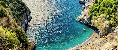 A coastal landscape with rocky cliffs, clear turquoise waters, and a narrow beach.