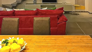 En moderne stue med en rød sofa, et træspisebord med citroner, en trappe og et fjernsyn.