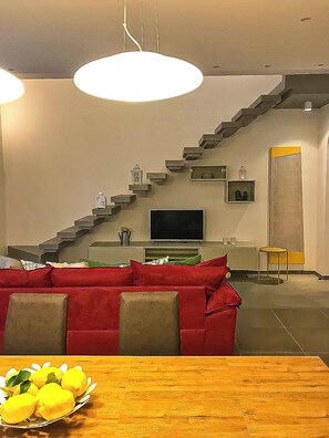 Ein modernes Wohnzimmer mit einem roten Sofa, einem Holzesstisch mit Zitronen, einer Treppe und einem Fernseher.