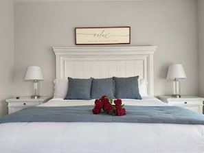 A bedroom with a white headboard, two bedside tables with lamps, a bed with grey bedding, and a framed sign above the bed. - Lake Taneycomo Waterfront | Stunning Views | 3BR (Branson)