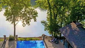 Piscina con jacuzzi, rodeada de árboles y vistas a un lago.