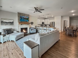 A modern living room with a fireplace, a sofa, a TV, and a dining area with wooden chairs and a table. - Lake Taneycomo Waterfront | Stunning Views | 3BR (Branson)