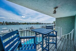 A wooden deck with a table and chairs overlooking a marina with boats and houses in the background.