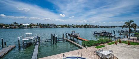 A swimming pool with a dock, a boat, and a view of a marina with houses in the background.