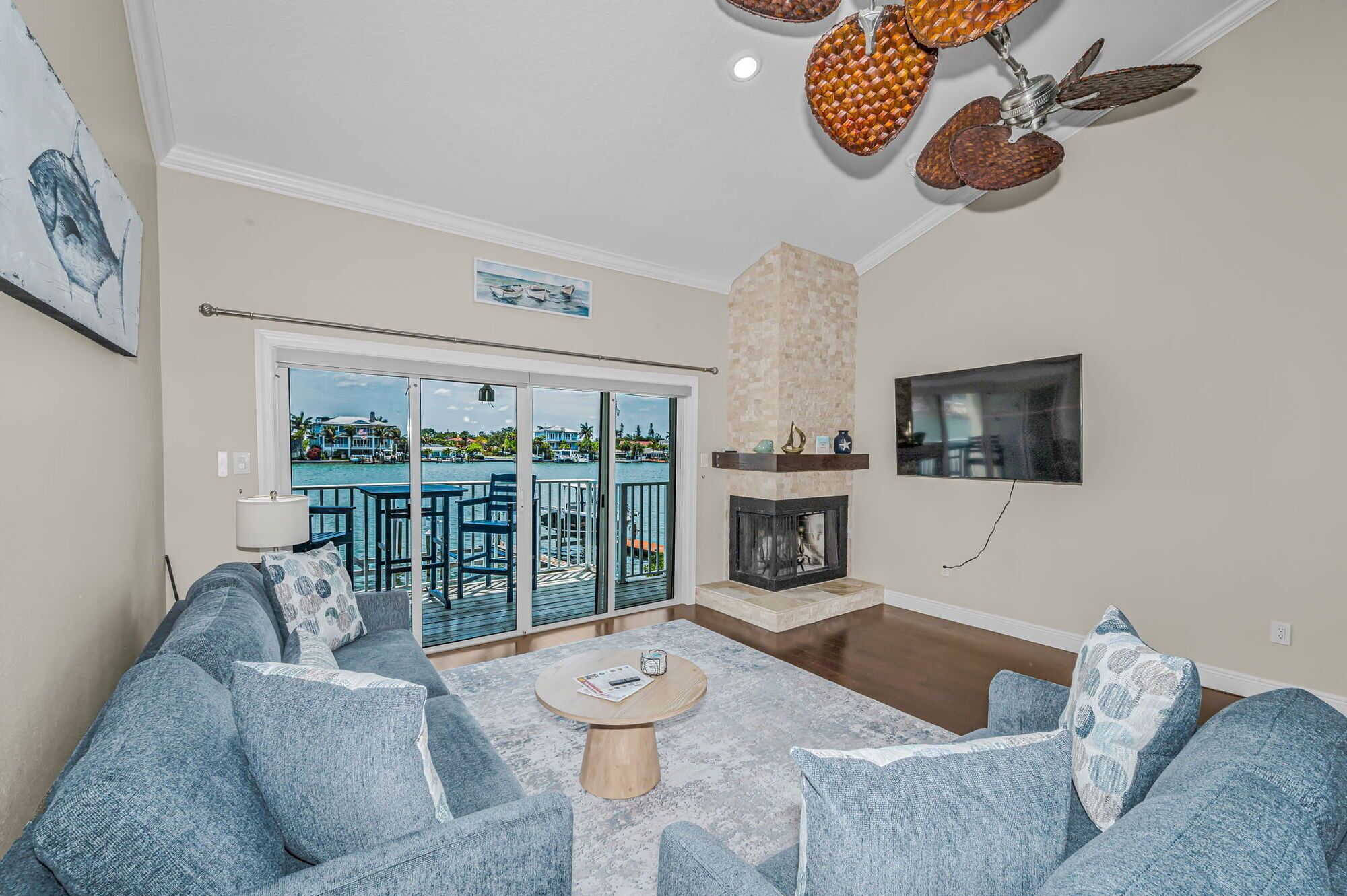 Un salon avec une cheminée, un balcon offrant une vue sur l’eau et un ventilateur de plafond.