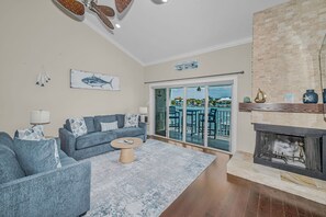 A living room with a sofa, coffee table, fireplace, and a view of the ocean through a sliding door.
