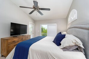 Ein Schlafzimmer mit Bett, Fernseher, einem Holzkasten, Deckenventilator und einem Balkon mit Jalousien.