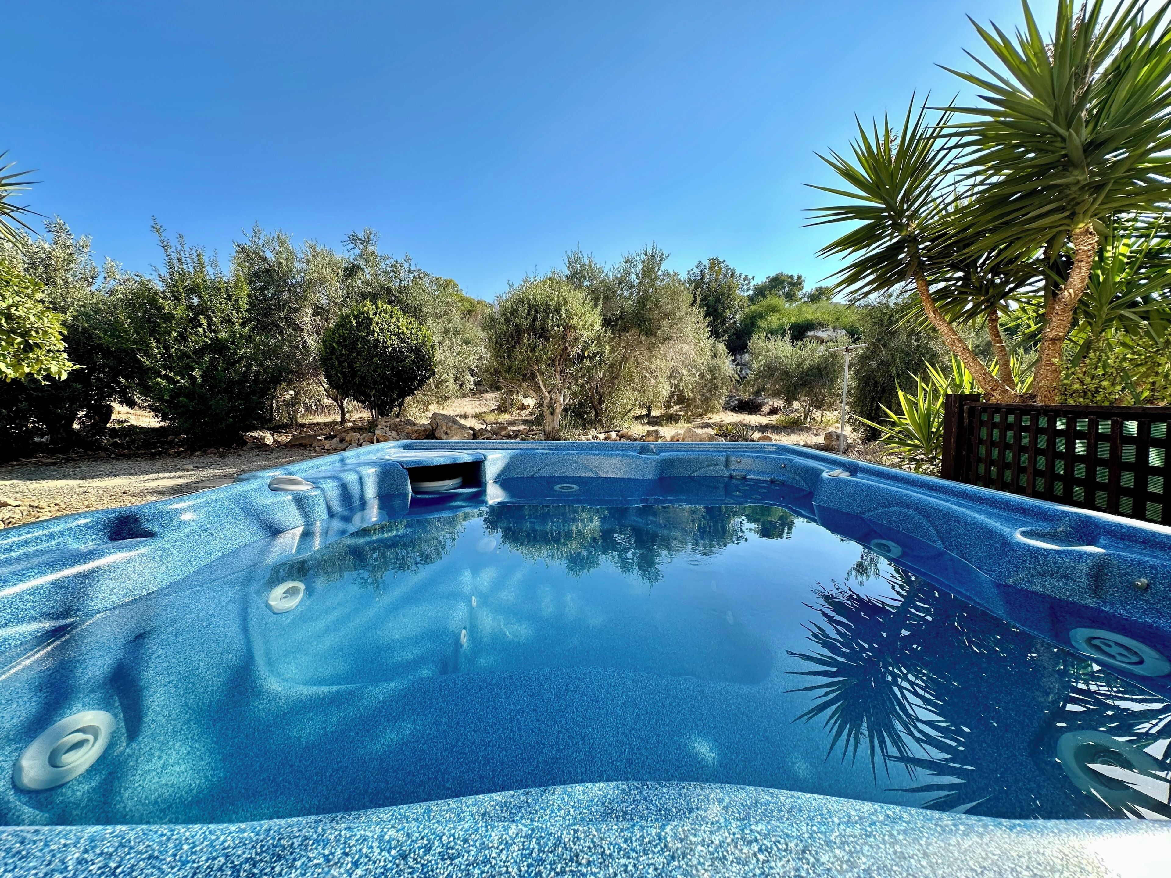Una piscina azul cristalina con textura de guijarros, rodeada de árboles y un paisaje rocoso.