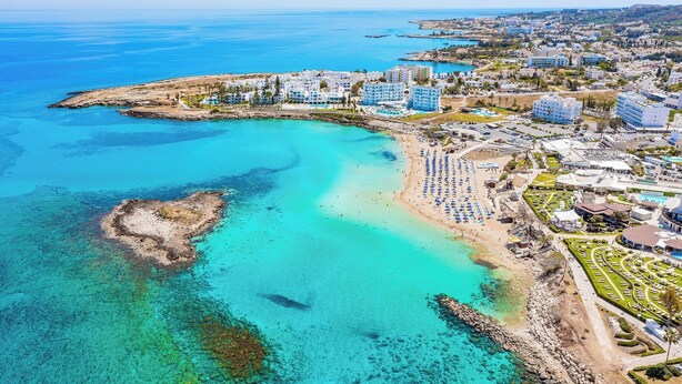 Eine Luftaufnahme eines Küstenresorts mit Strandvillen, einem Sandstrand und klarem, blauem Wasser.