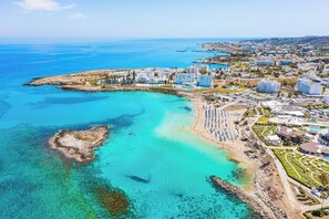 Una vista aerea di una località balneare con ville affacciate sulla spiaggia, una spiaggia sabbiosa e acque cristalline.