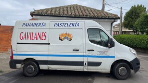 Ein weißer Van mit der Aufschrift 'PANADERÍA GAVILANES' und 'PASTELERÍA', geparkt in einer Straße.
