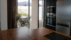 Eine moderne Küche mit eingebautem Ofen und Kühlschrank, einem Holztisch und einer Glastür, die auf eine Terrasse mit Tisch und Stühlen hinausführt.