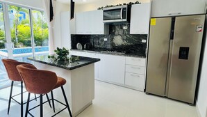 Een moderne keuken met witte kastjes, een roestvrijstalen koelkast, een magnetron en een bargedeelte met twee stoelen.