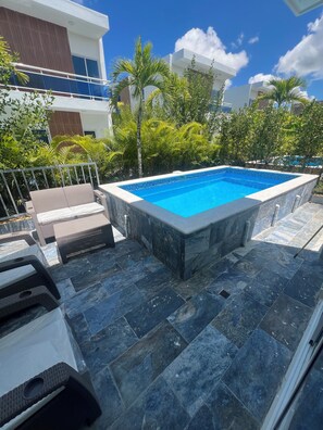 Ein Schwimmbecken mit gefliestem Deck, umgeben von Grünflächen und modernen Gebäuden.