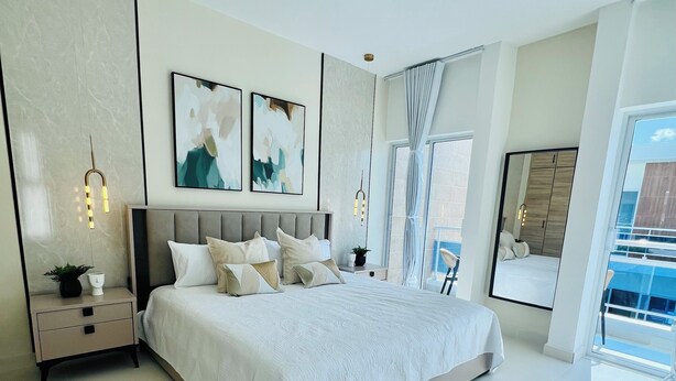 Een moderne slaapkamer met een groot bed, nachtkastjes, wanddecoratie en uitzicht op de natuur.