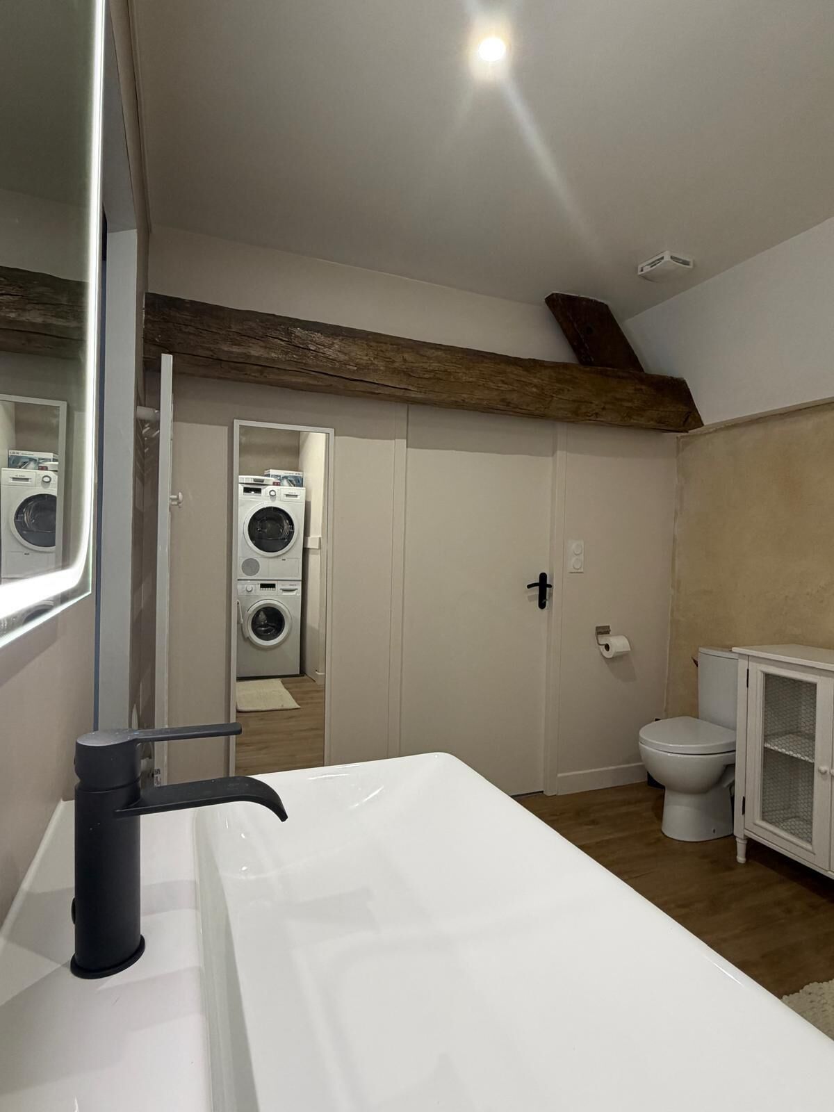 Ein Badezimmer mit einem weißen Waschbecken, einer Toilette und einer Waschmaschine im Hintergrund.