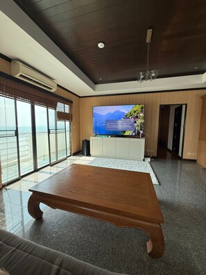 A modern living room with a large flat-screen TV, a wooden coffee table, and a view of the sea through large windows.