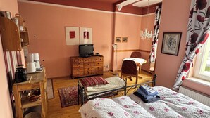 A bedroom with a bed, a wooden dresser, a desk with a computer, a chair, and a window with curtains. - Engelapartment in the Villa Schulenburg (Putbus)