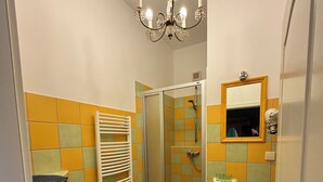 A bathroom with a shower, toilet, sink, and a chandelier. - Engelapartment in the Villa Schulenburg (Putbus)
