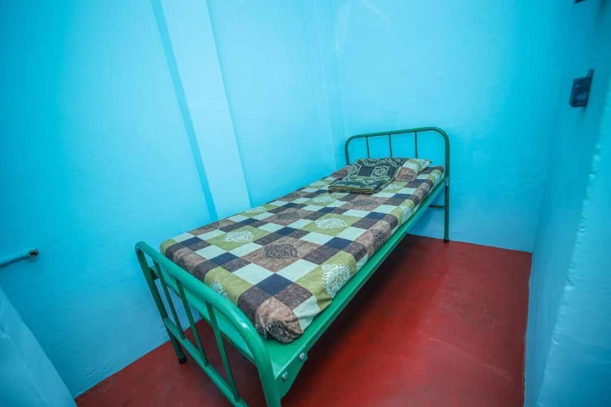 A single-bed room with a metal frame, a checkered bedspread, and a red floor.