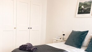 Hotellihuone, jossa on sänky, yöpöytä, lamppu ja seinällä oleva kehystetty kuva.