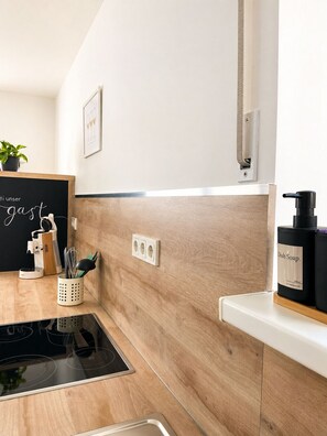 Eine moderne Küche mit Holzrückwand, einer Tafel mit Schrift, einer Kaffeemaschine und einer Flasche Geschirrspülmittel auf einem Regal.