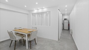 A modern dining area with a wooden table and four chairs, a window with curtains, and a kitchen in the background. - 🏡 Charming renovated 2-room apartment - Ideal location behind the Martinez in Cannes (Cannes)