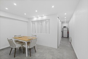 Ein moderner Essbereich mit einem Holztisch und vier Stühlen, einem Fenster mit Vorhängen und einer Küche im Hintergrund.