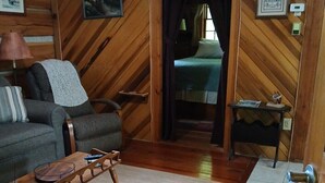 A wooden interior with a sofa, a small table, a bed, and a door leading to another room. - Cozy 1-bedroom cabin in gorgeous Maggie Valley with AC (Maggie Valley)