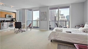 Ein modernes Hotelzimmer mit einem großen Bett, einem Schreibtisch, einem Sessel, Blick auf die Stadt und einer Küchenzeile.