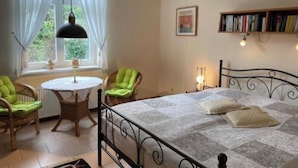 Une chambre à coucher avec un lit, deux chaises, une table ronde, une bibliothèque et une fenêtre avec des rideaux.