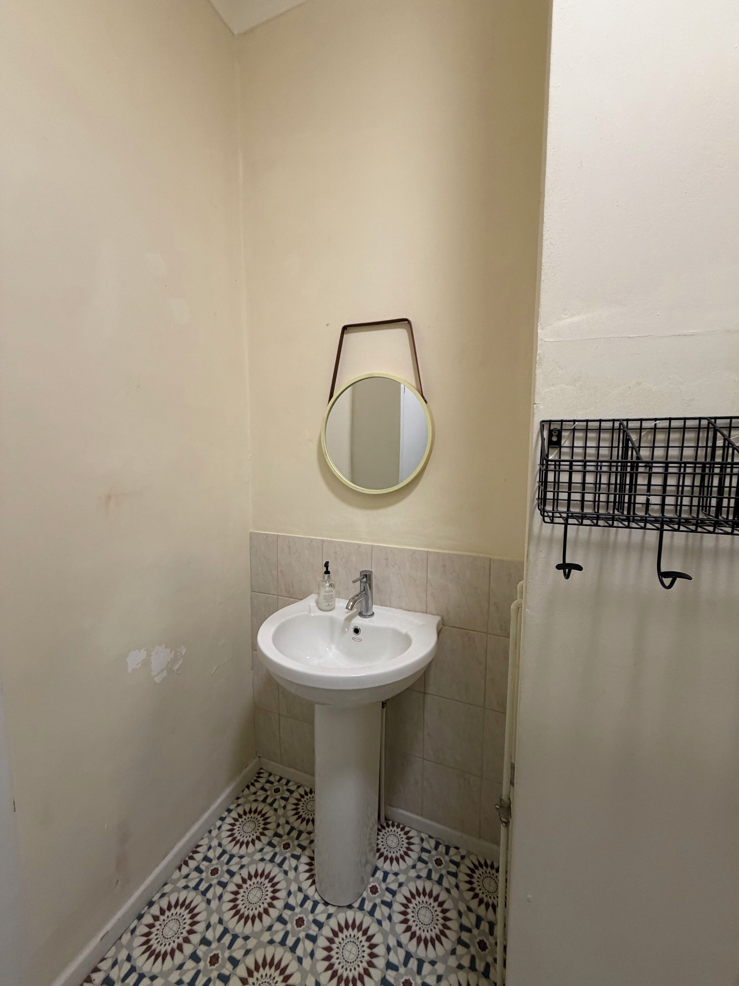 A bathroom with a pedestal sink, a round mirror, and a tiled floor.