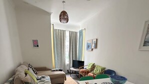 A living room with a sofa, a dining table with chairs, a TV, and a window with curtains.