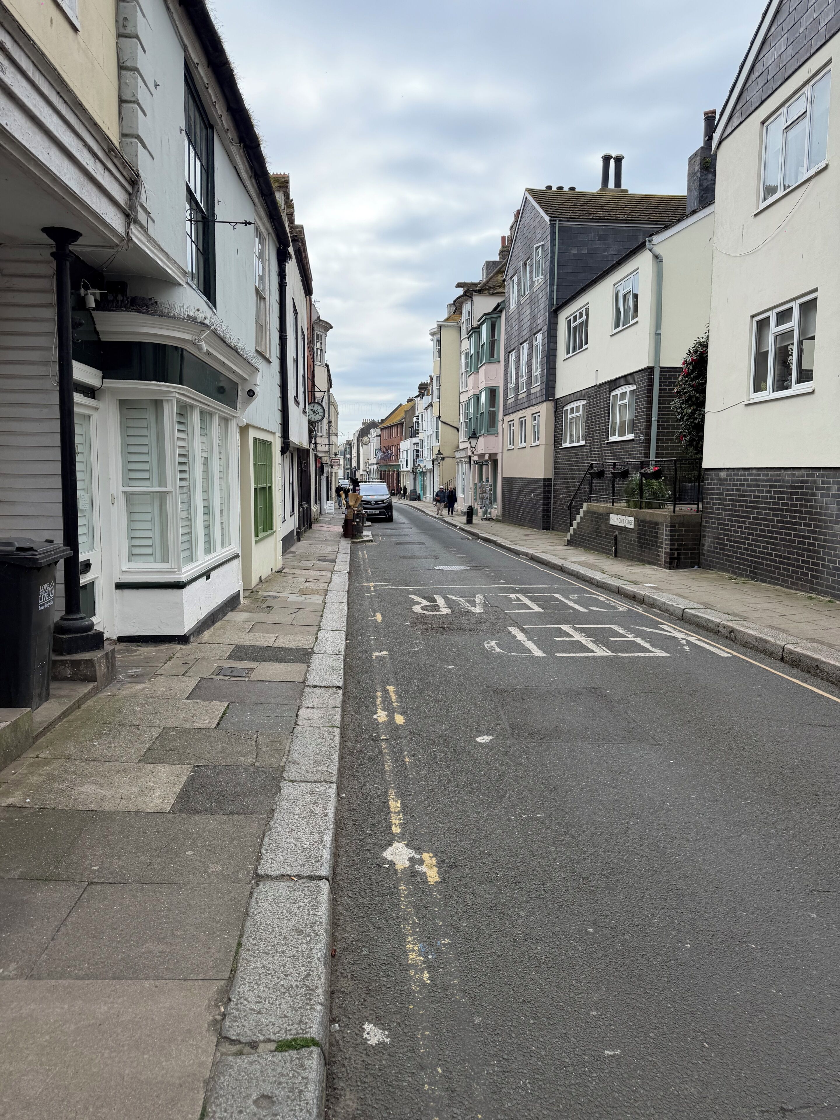 Une rue étroite en milieu urbain, bordée d’immeubles d’habitation à plusieurs étages, avec une chaussée dégagée et un trottoir pour les piétons.