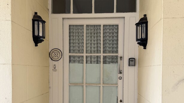 A white door with a glass panel, a doormat with seahorse designs, and two wall-mounted lanterns.