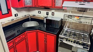 Una cocina con gabinetes rojos, un lavamanos de acero inoxidable, un microondas y una estufa a gas.