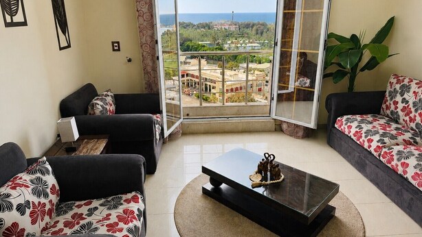 Una sala de estar con dos sofás, una mesa de centro y un ventanal con vistas a edificios y zonas verdes.