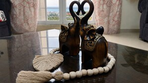 Una figurita de madera de elefante con una parte superior en forma de corazón, un collar de cuentas y un objeto tejido sobre una mesa.
