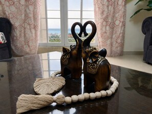 Une figurine d’éléphant en bois, surmontée d’un cœur, portant un collier de perles, et un objet tissé posé sur une table.