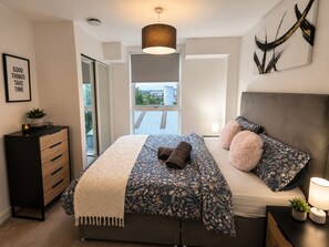 Ein modernes Schlafzimmer mit Bett, Nachttisch, Lampe und Blick durch ein Fenster.