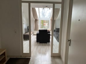 Une pièce dotée d’une porte-fenêtre coulissante donnant sur un balcon, d’un canapé noir et d’un ventilateur de plafond.