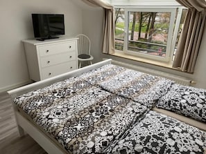 A bedroom with a bed, a TV on a dresser, a chair, and a window with curtains.