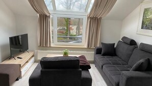 A modern living room with a sofa, a TV, a small table, and a window with curtains. - Fantastic vacation apartment "Haus am Meer" in Bad Zwischenahn with top location by the sea (Bad Zwischenahn)