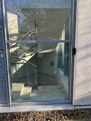 Un bâtiment moderne doté d’une entrée en verre, de rampes en métal et d’un escalier menant à un niveau supérieur.
