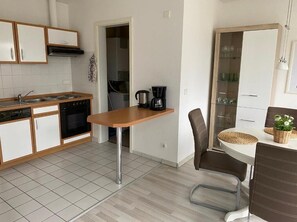 A compact kitchen with a stove, sink, and coffee maker. There is a dining area with a table and chairs.