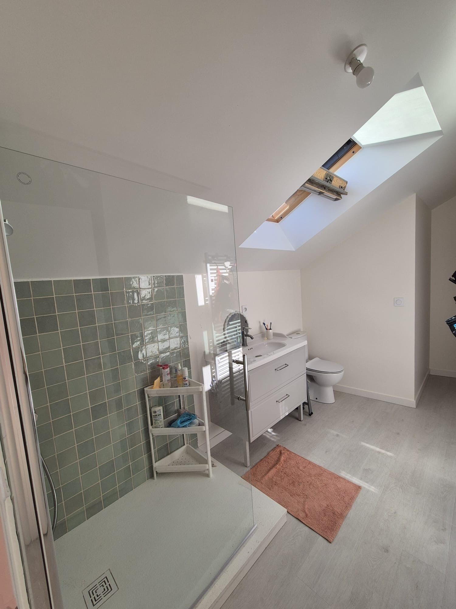 A modern bathroom with a skylight, a glass shower enclosure, and a white vanity.