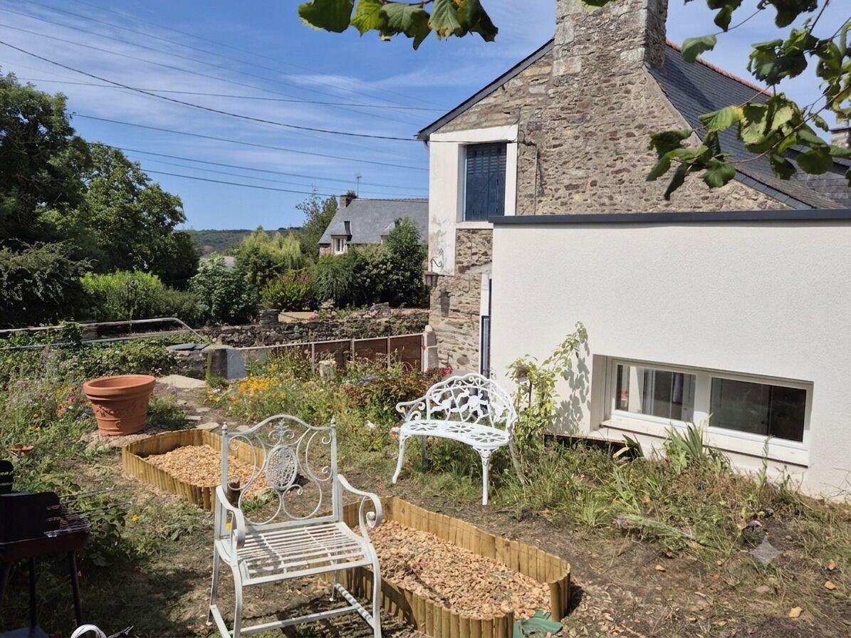 A garden with a white metal bench, a large terracotta pot, and a stone wall adjacent to a building with a window.