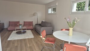 A modern living room with a grey sofa, a round coffee table, and a white table with orange chairs.