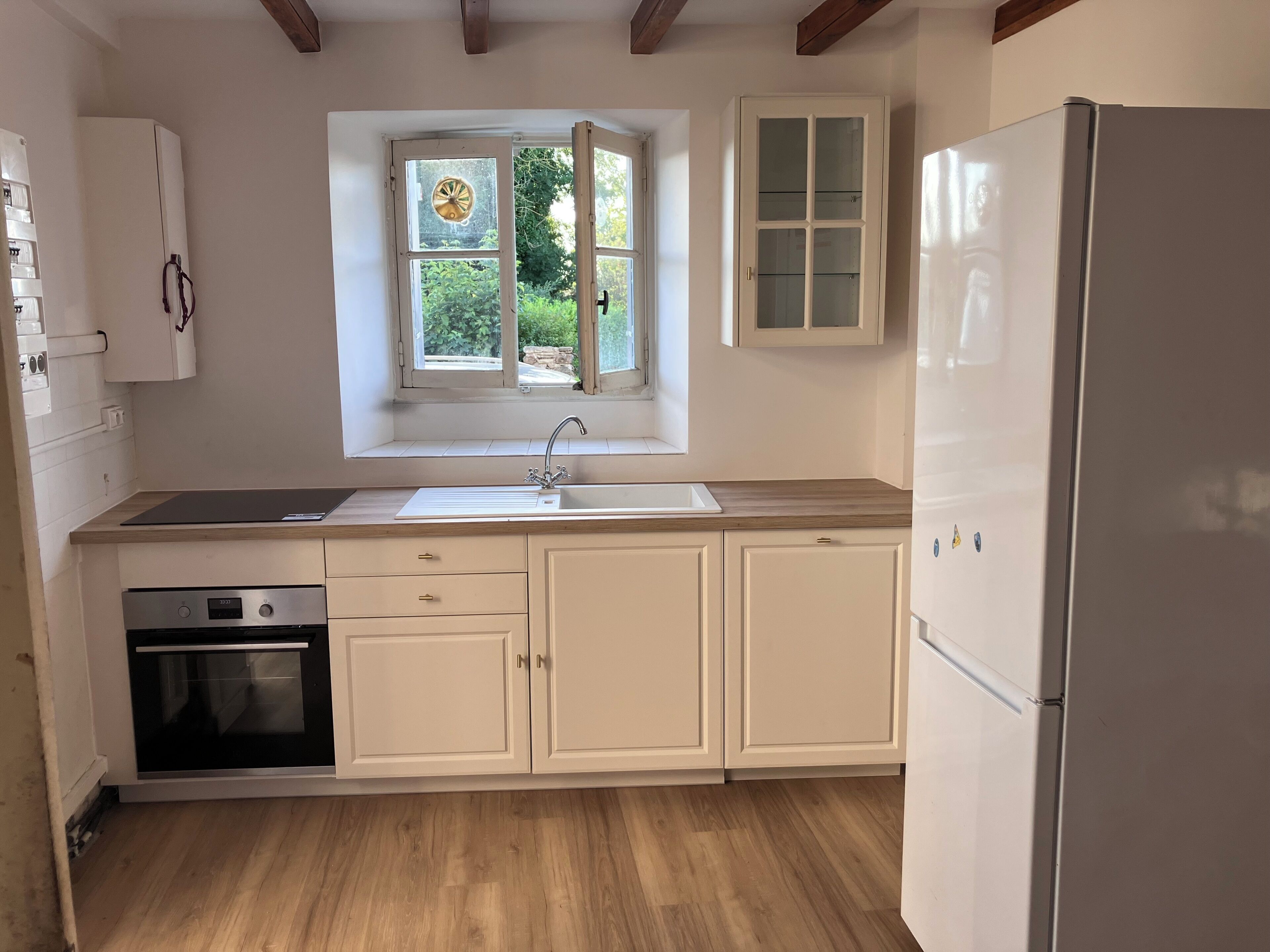 A kitchen with a window, a sink, cabinets, and a refrigerator.