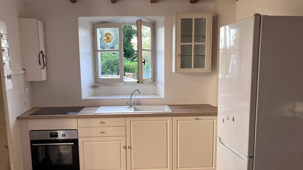 A kitchen with a window, a sink, cabinets, and a refrigerator.